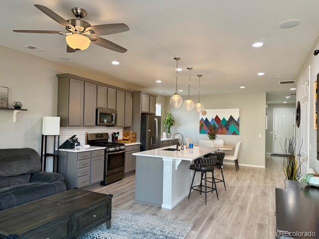 kitchen with a center island with sink, a sink, gray cabinetry, stainless steel appliances, and a kitchen breakfast bar