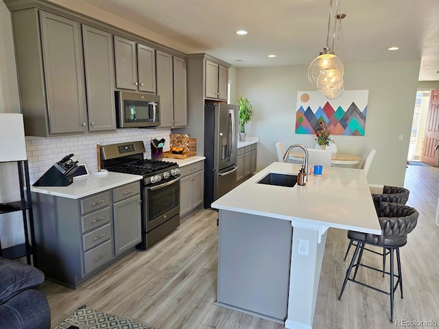 kitchen featuring a breakfast bar area, gray cabinets, a sink, appliances with stainless steel finishes, and tasteful backsplash