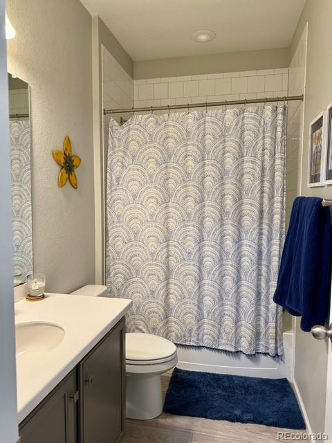 bathroom featuring toilet, vanity, shower / tub combo with curtain, and wood finished floors