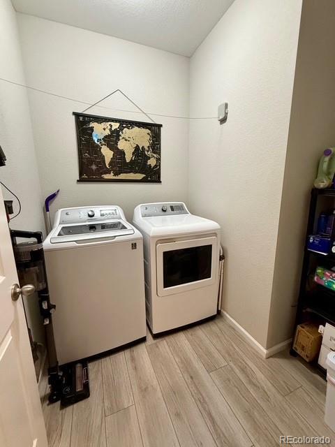 washroom with baseboards, light wood-style flooring, laundry area, and washing machine and clothes dryer