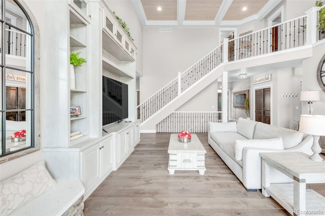 living room featuring beam ceiling, light hardwood / wood-style floors, wooden ceiling, and a towering ceiling