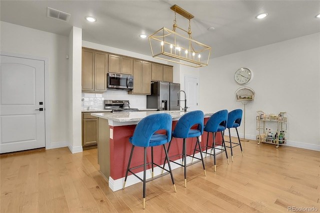 16818 E 119th Ave Unit A, Commerce City, CO 80022 - kitchen with stainless steel appliances, light wood-style floors, a center island with sink, decorative backsplash, and a breakfast bar