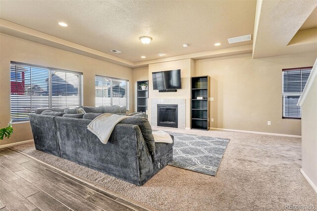 7963 Bonfire Trl, Fountain, CO 80817 - carpeted living room featuring a textured ceiling, baseboards, a tiled fireplace, a raised ceiling, and recessed lighting
