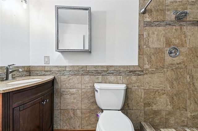 bathroom featuring a tile shower, a wainscoted wall, toilet, vanity, and tile walls