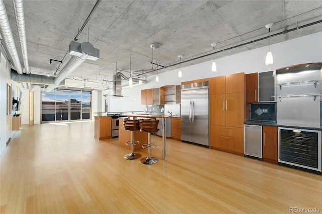 kitchen featuring beverage cooler, stainless steel appliances, wall chimney range hood, and brown cabinets