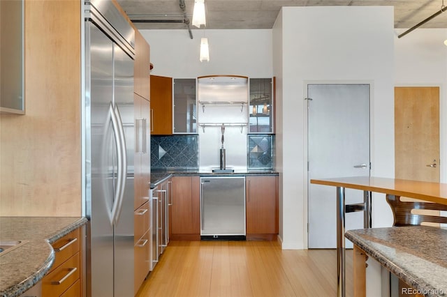 kitchen with built in fridge, refrigerator, backsplash, brown cabinets, and light wood finished floors