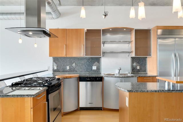 kitchen with island exhaust hood, light wood finished floors, appliances with stainless steel finishes, a sink, and dark stone countertops