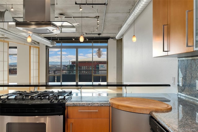 kitchen with island range hood, stainless steel range with gas stovetop, brown cabinets, dark stone countertops, and rail lighting