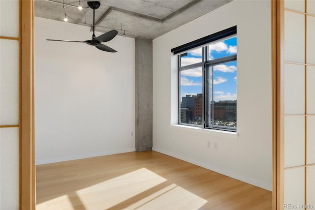 unfurnished room featuring a city view, ceiling fan, light wood-style flooring, and baseboards