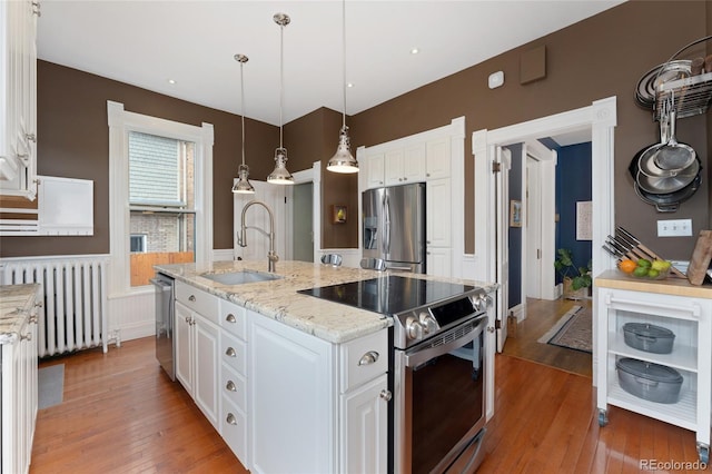 1154 N Clarkson St, Denver, CO 80218 - kitchen with radiator heating unit, appliances with stainless steel finishes, light wood-style flooring, white cabinets, and a kitchen island with sink