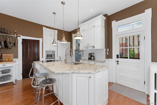 1154 N Clarkson St, Denver, CO 80218 - kitchen with light wood-style flooring, wainscoting, stainless steel microwave, white cabinets, and tasteful backsplash
