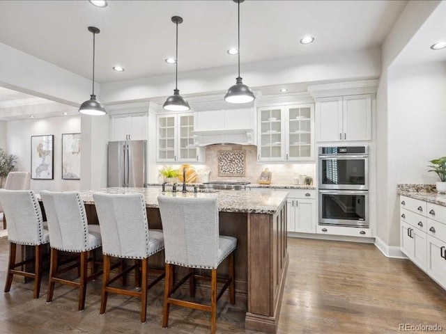 kitchen with white cabinets, hanging light fixtures, an island with sink, and appliances with stainless steel finishes