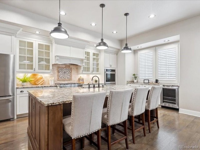 kitchen with a kitchen island with sink, wine cooler, appliances with stainless steel finishes, dark hardwood / wood-style flooring, and white cabinetry