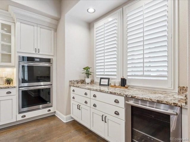 kitchen with white cabinets, light stone countertops, stainless steel double oven, and wine cooler