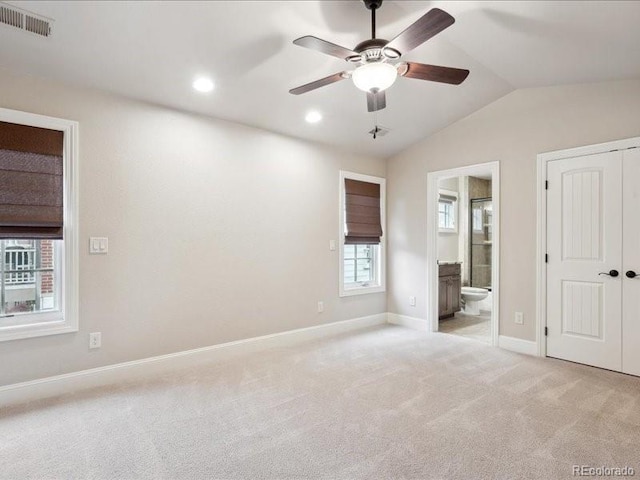 unfurnished bedroom with ceiling fan, multiple windows, light carpet, and ensuite bath