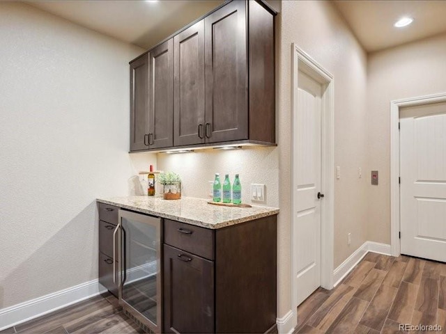 bar featuring dark brown cabinets, light stone counters, dark wood-type flooring, and wine cooler