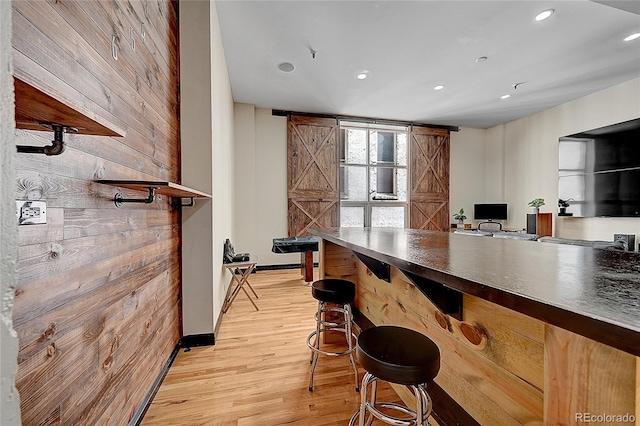 bar with a barn door, wood walls, and light hardwood / wood-style flooring