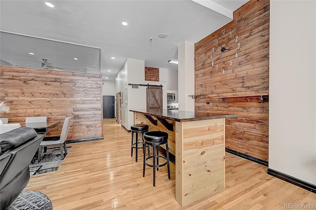 kitchen with a breakfast bar area, light hardwood / wood-style flooring, wood walls, and a barn door