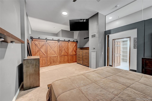 bedroom featuring light colored carpet, ensuite bathroom, and a barn door