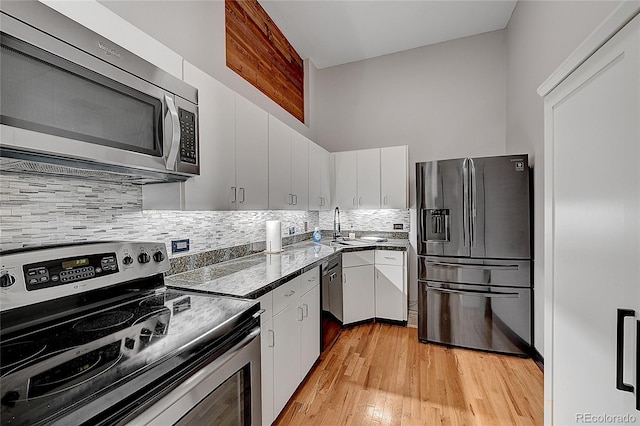 kitchen featuring appliances with stainless steel finishes, light wood-type flooring, white cabinetry, and decorative backsplash