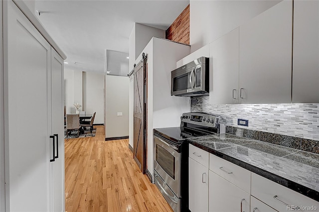 kitchen with stainless steel appliances, white cabinetry, light hardwood / wood-style floors, and a barn door