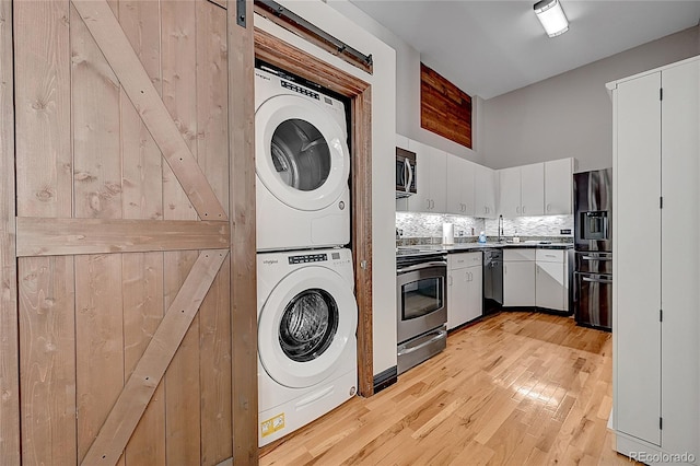 kitchen with appliances with stainless steel finishes, stacked washing maching and dryer, white cabinetry, backsplash, and light wood-type flooring