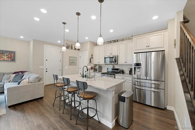 kitchen featuring sink, dark wood-type flooring, stainless steel appliances, a center island with sink, and decorative light fixtures