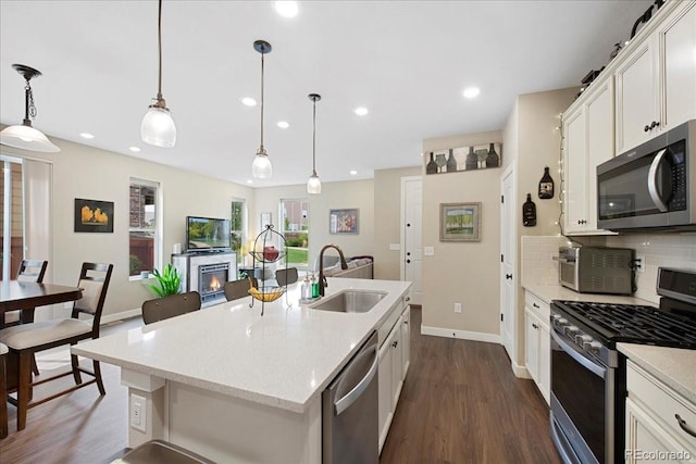 kitchen featuring a kitchen island with sink, sink, hanging light fixtures, and appliances with stainless steel finishes