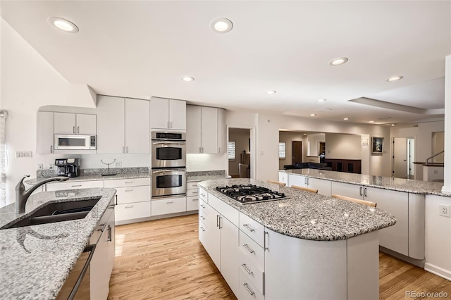 kitchen featuring light stone countertops, stainless steel appliances, sink, white cabinets, and light hardwood / wood-style floors