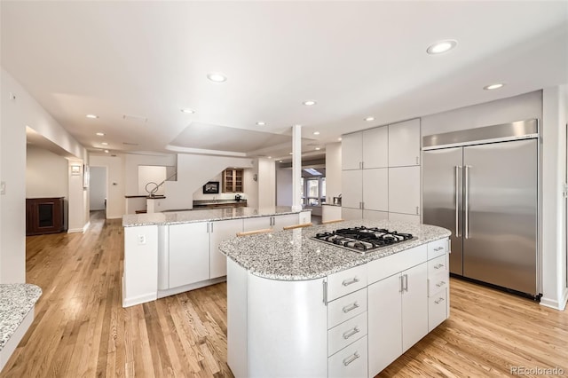 kitchen featuring a kitchen island, appliances with stainless steel finishes, light hardwood / wood-style floors, light stone counters, and white cabinetry