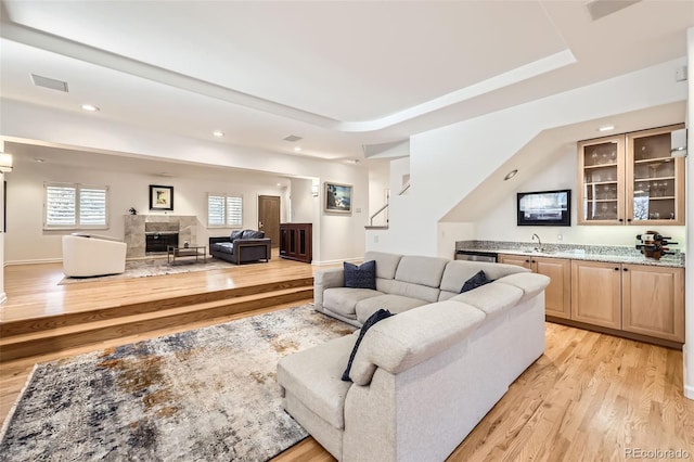 living room featuring a tray ceiling, a tile fireplace, and light hardwood / wood-style flooring