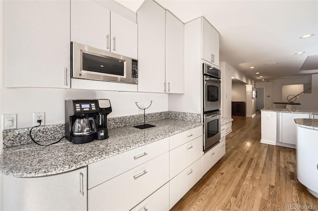 2 Elm St, Denver, CO 80220 - kitchen featuring appliances with stainless steel finishes, light wood-style flooring, white cabinets, recessed lighting, and light stone countertops