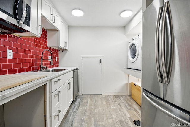 6948 W 70th Ave, Arvada, CO 80003 - kitchen with decorative backsplash, washer / clothes dryer, appliances with stainless steel finishes, a sink, and light wood-style floors