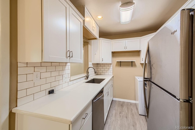 kitchen with sink, backsplash, white cabinetry, appliances with stainless steel finishes, and light hardwood / wood-style floors