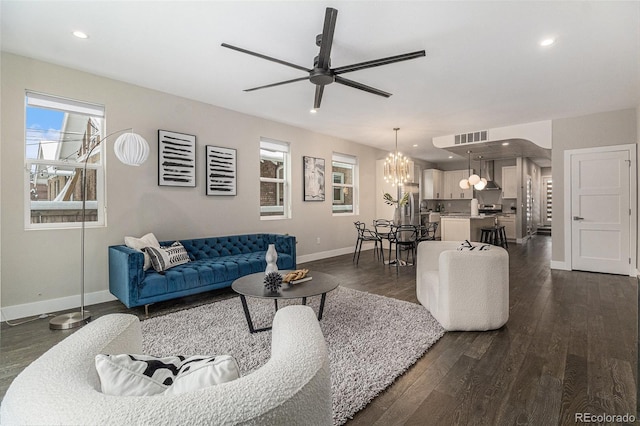 living room featuring ceiling fan with notable chandelier and dark wood-type flooring