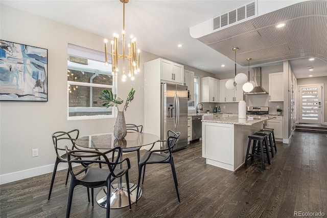 kitchen with appliances with stainless steel finishes, decorative light fixtures, white cabinets, a center island, and wall chimney range hood