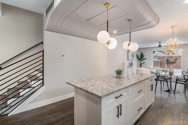 kitchen featuring white cabinetry, decorative light fixtures, a center island, dark hardwood / wood-style floors, and light stone countertops