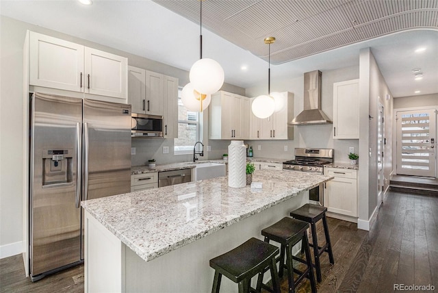 kitchen with a kitchen island, appliances with stainless steel finishes, pendant lighting, white cabinetry, and wall chimney exhaust hood