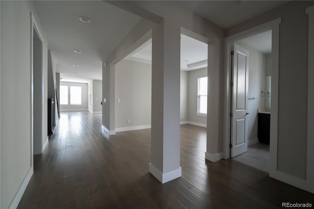 corridor featuring a wealth of natural light, baseboards, and dark wood-type flooring