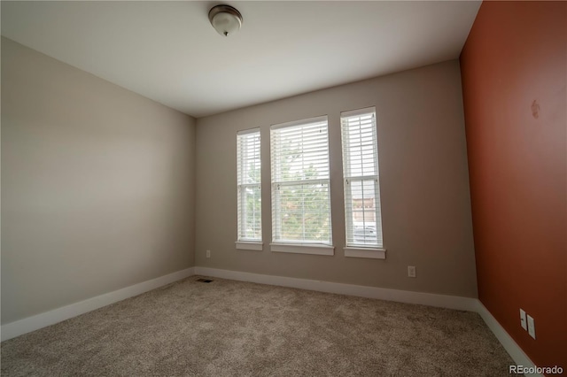 empty room with carpet, visible vents, and baseboards