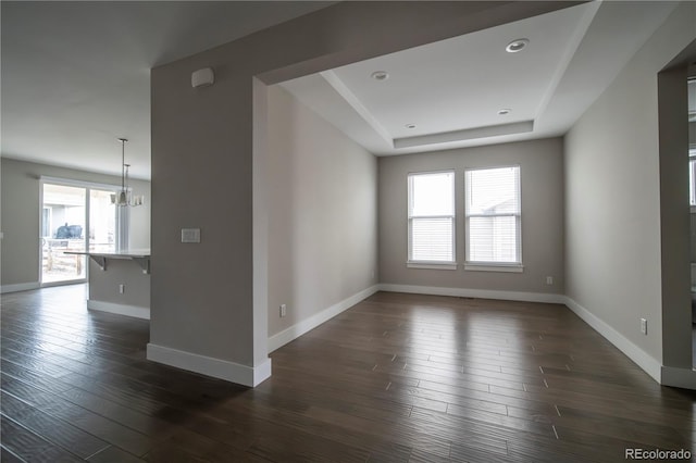 empty room featuring dark wood-style floors, a raised ceiling, a notable chandelier, and baseboards