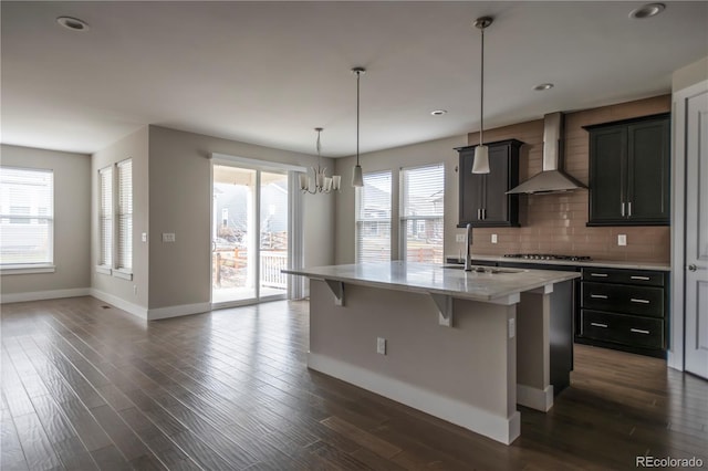 kitchen with a breakfast bar area, stainless steel gas cooktop, wall chimney range hood, backsplash, and dark wood-style floors