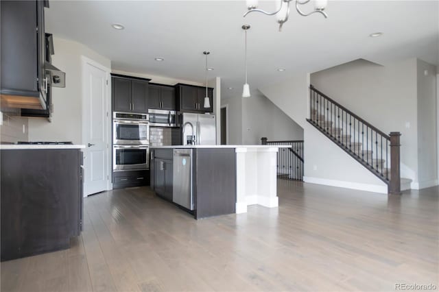 kitchen featuring pendant lighting, light countertops, appliances with stainless steel finishes, an island with sink, and wood finished floors