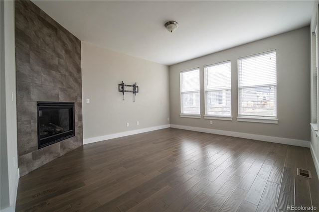 unfurnished living room with dark wood-style floors, baseboards, visible vents, and a tiled fireplace