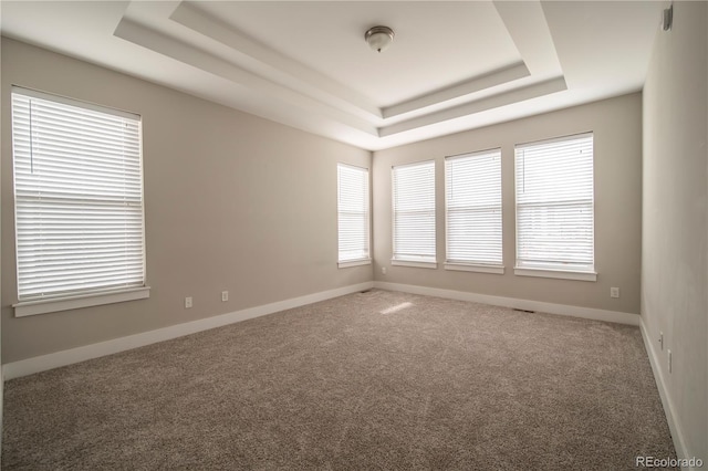 carpeted spare room featuring a tray ceiling and baseboards