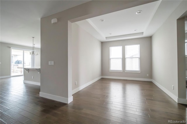 spare room featuring baseboards, dark wood-style floors, recessed lighting, a tray ceiling, and a chandelier
