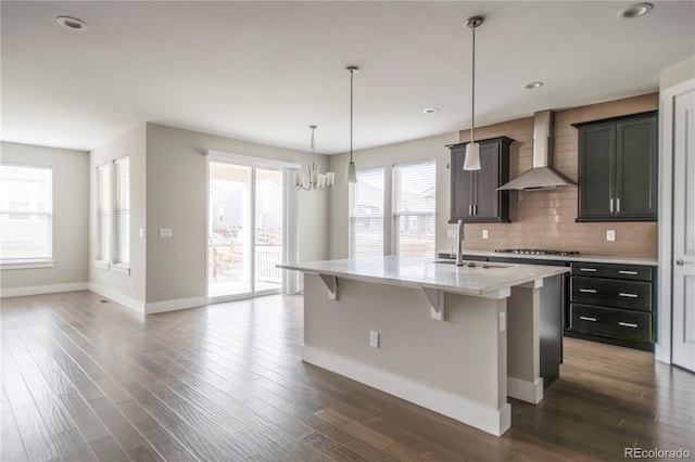 kitchen featuring baseboards, stainless steel gas cooktop, wall chimney range hood, and a kitchen breakfast bar