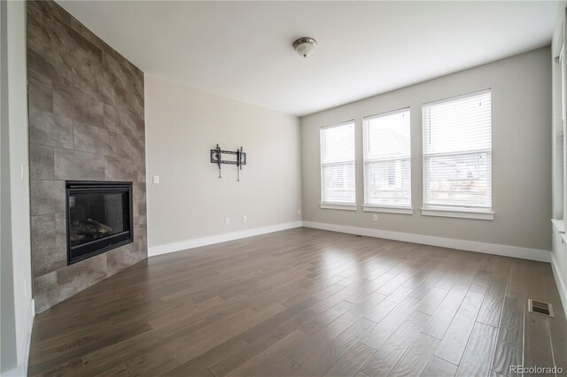 unfurnished living room featuring baseboards, dark wood finished floors, a tile fireplace, and visible vents