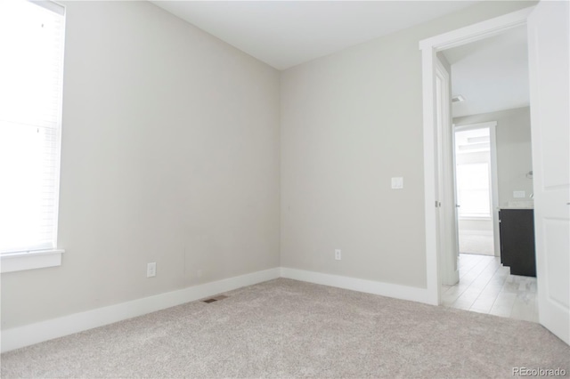 spare room featuring baseboards, visible vents, and light carpet
