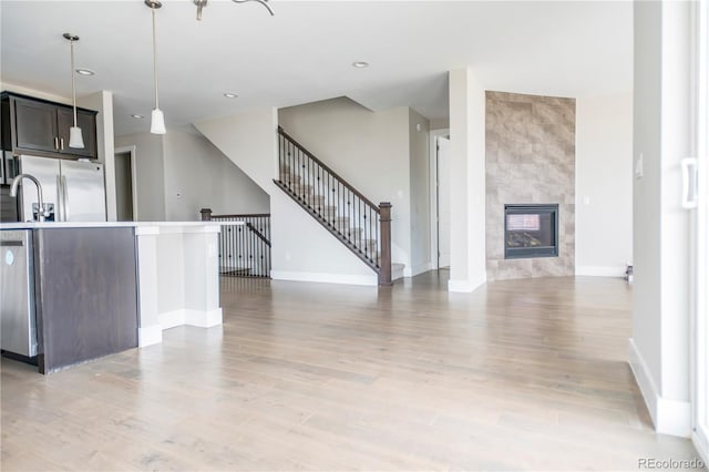 kitchen featuring baseboards, open floor plan, light wood-style flooring, appliances with stainless steel finishes, and decorative light fixtures